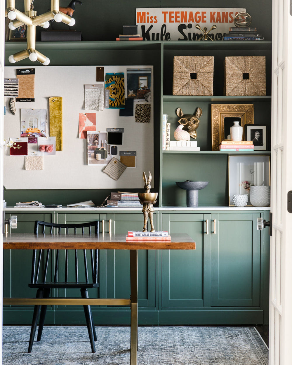 Green home office with built-in shelves, a wood desk and black chair.
